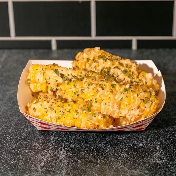 Elote-style corn ribs, coated in creamy sauce and sprinkled with herbs, in a striped paper tray.