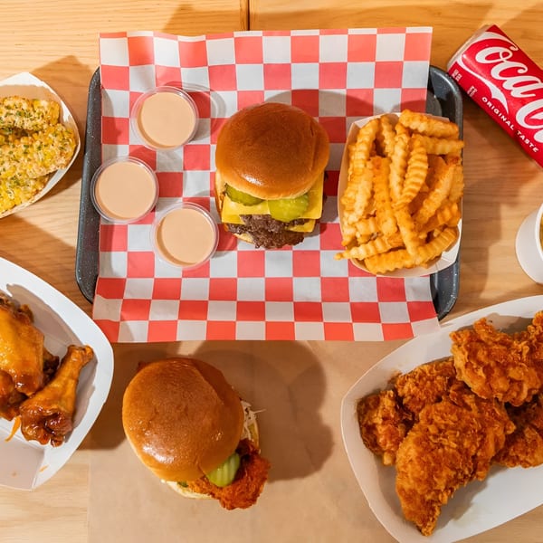Overhead view of a fast-food meal with burgers, fries, chicken wings, mac and cheese, and corn.