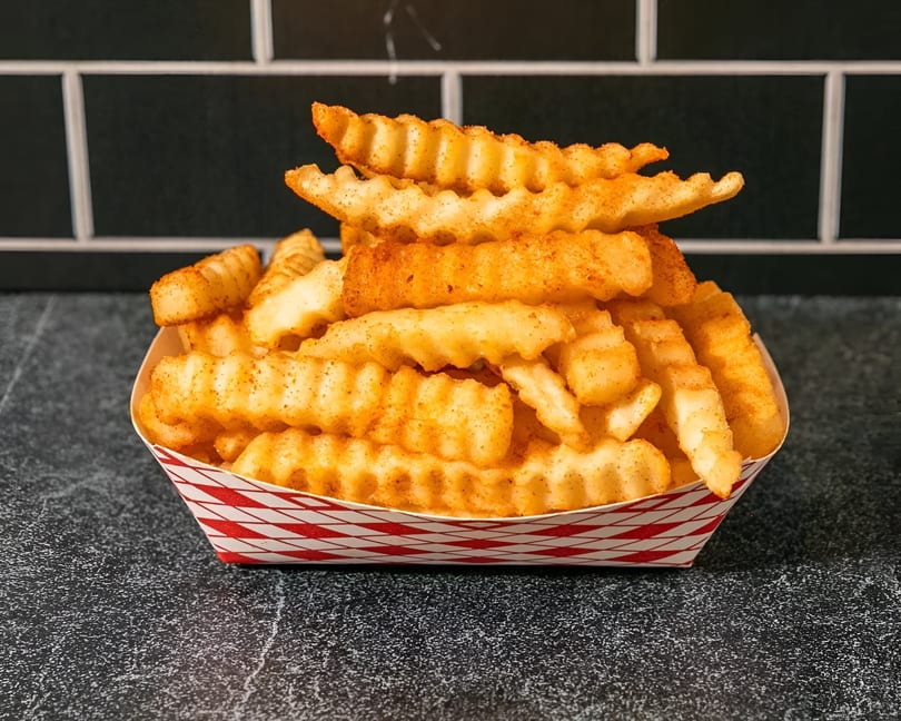 Crinkle-cut fries seasoned with red spices, served in a red and white checkered paper tray.