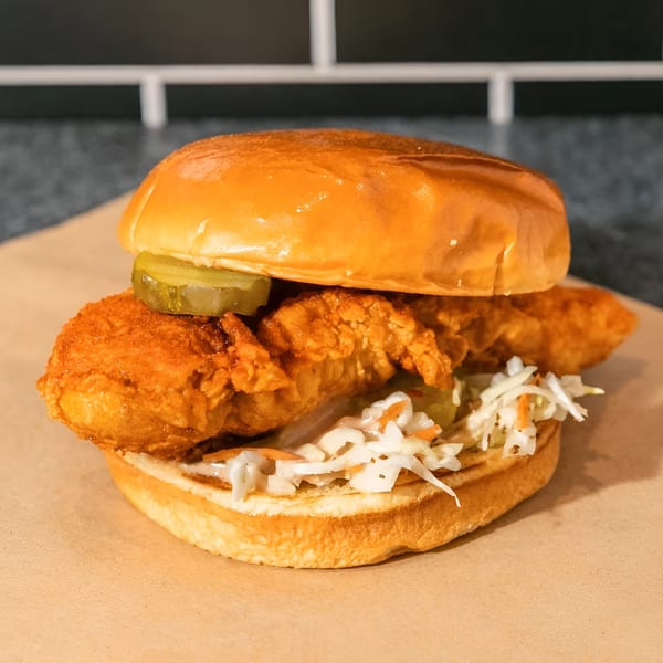 Crispy fried chicken sandwich with pickles and coleslaw on a brioche bun, on a brown paper.