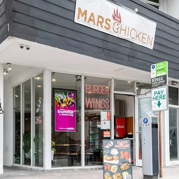 Exterior of Mars Hot Chicken restaurant with a banner, neon signs, and a menu board.