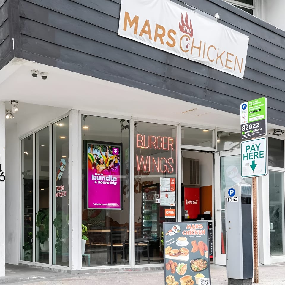 Exterior of Mars Hot Chicken restaurant with a banner, neon signs, and a menu board.